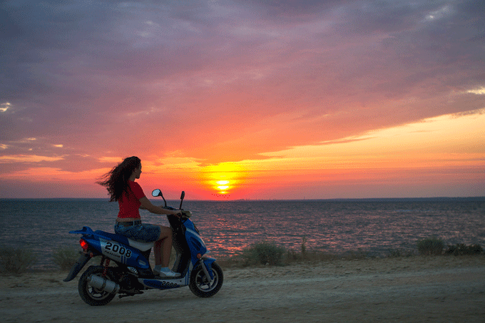mulher pilotando uma scooter na praia ao por do sol